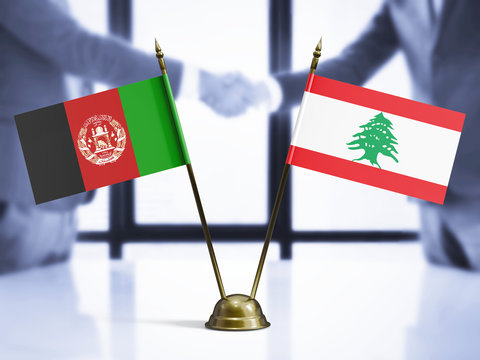 Lebanon and Afghanistan mini table flags on white wooden desk. Diplomatic background with men shaking hands, international relations and agreements.