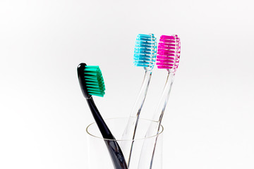 Toothbrushes of different colors in a glass beaker on a white background.