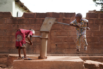 Small African Boy Trying to Pump Water from the Village Well - obrazy, fototapety, plakaty