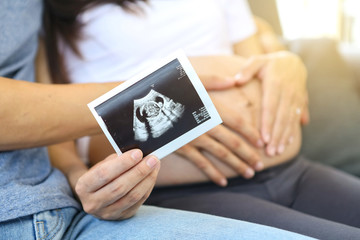 Mother and father holding the baby ultrasound photo. Mum and dad are showing off ultrasound images of their fetus. Heart shaped hand. New born.
