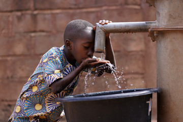 Young African Boy Drinking Water From The Community Borehole Hand Pump