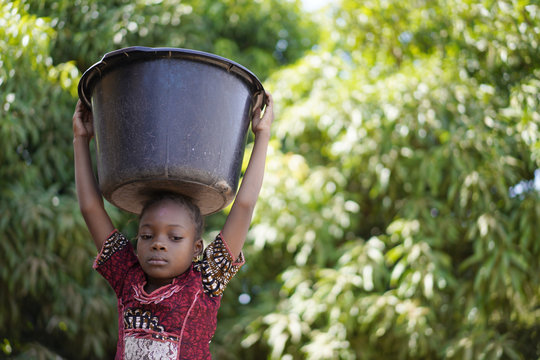 Troubled Tiny African Girl Trying to Balance A Heavy Water Bucket On Her Head