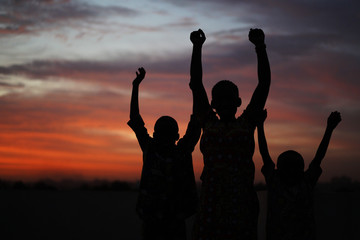 Three African Siblings Raising Their Hands Against A Colorful Evening Sky