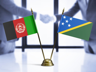 Solomon Islands and Afghanistan mini table flags on white wooden desk. Diplomatic background with...