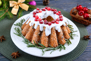 Christmas fruit cake on white plate. Homemade fruitcake decorated with rosemary, powdered sugar and lingonberry on a wooden rustic background