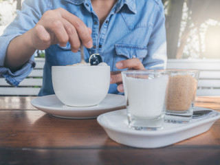 Close-up hand using a spoon stirring coffee in white ceramic cup.