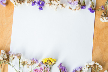Multicolored dried flowers on wooden background, colorful limonium statice plant with copy space, blank white paper with place for text