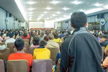 Backside view of spectators standing in a gathering in the back of auditorium full of people. Selective focus.