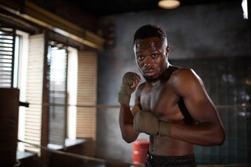 Naklejka na ściany i meble Portrait of African young muscular man standing and posing at camera while training in gym