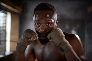 Portrait of African young man in boxing gloves looking at camera during sports training