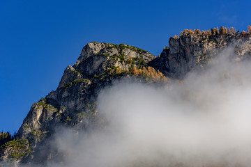 Fototapeta na wymiar Dolomite mountains with low clouds in Italian Alps / During autumn in sunny day with blue sky