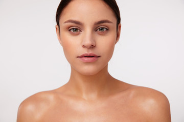 Close-up of beautiful young brunette green-eyed woman with natural makeup looking sincerely at...