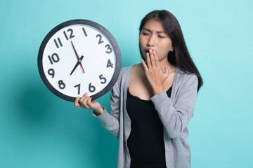 Sleepy young Asian woman with a clock in the morning.