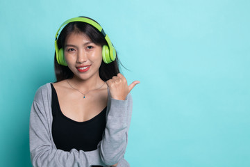 Pretty asian girl listening music with her headphones point to copy space with her thumb.