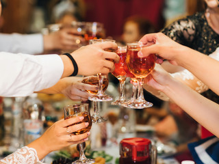 hands of a group of people clinking and toasting glasses of red wine at a festive party in a restaurant