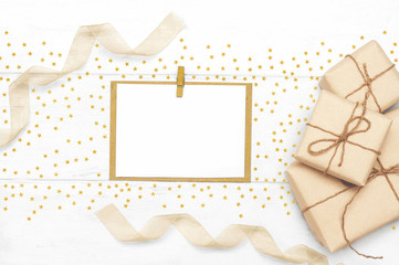 Gift boxes wrapped in eco paper and rope with golden stars, ribbons blank postcard on a white wooden background boards. Gifts for holiday concept. Top view. Flat lay