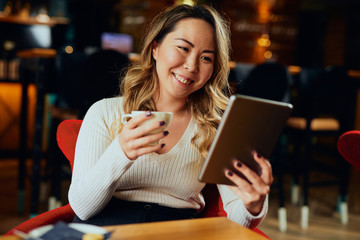 Beautiful Asian woman drinking coffee and looking at her tablet	