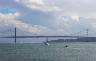10/21/2018 - Lisbon, Portugal: Famous suspension bridge over river Tejo with sailboats in Lisbon. Lisbon landmark. Regatta concept. Navigation and water sport concept. Vessel boats race.