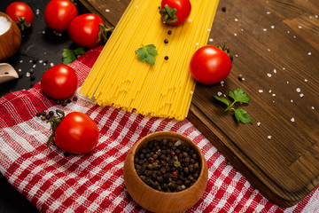 wooden cutting board and fresh red cherry tomatoes, beside a tied bundle of long raw spaghetti