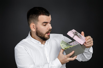 portrait of handsome bearded man in white shirt opens gift box with money isolated on black background