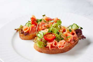 two sandwiches with ham, baked tomatoes, cucumbers, lettuce, herbs and spices