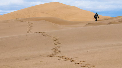 Fußspuren auf Sanddüne mit weglaufender Person im Hintergrund