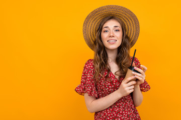 studio portrait of a charming stylish smiling girl in a hat with a paper cup on an orange background