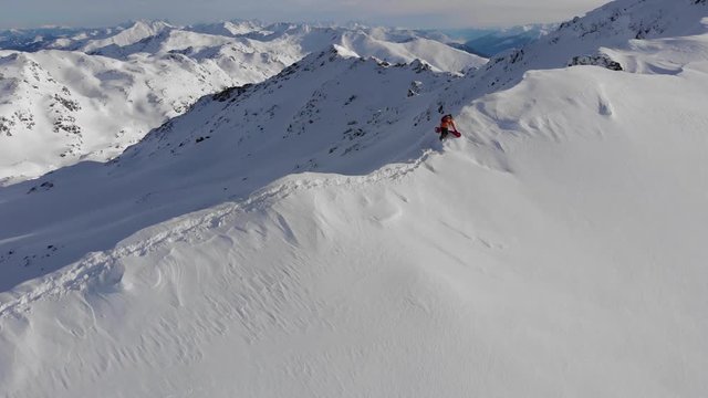 Beautiful drone shot of snowboarder walking on thin ridge towards the summit
