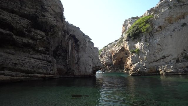 Stunning hidden lagoon secluded by tall cliffs that hide it from the open ocean. Cliff faces worn by weather wrap around a small beach and warm clear water of the ocean in Croatia.