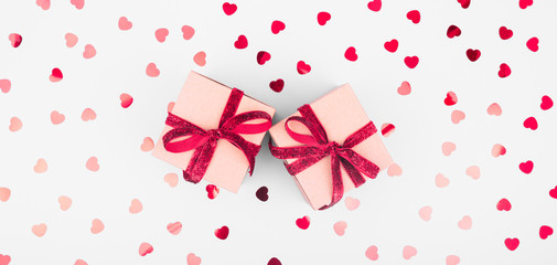 Craft box with red ribbon bow and glitter heart confetti. Valentine day and eco-friendly wrapping concept. Trendy minimalistic flat lay design background. Wide screen banner format