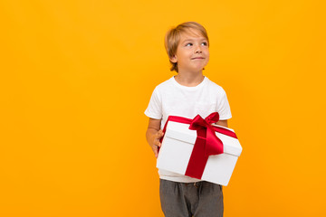 boy holds a box with a red ribbon and looks away on a yellow background