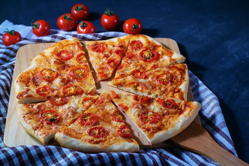 Freshly baked homemade pizza Margherita cut into pieces lies on a black background.