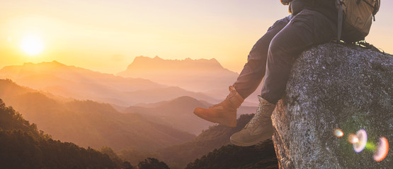 Successful male legs of traveler sitting on a high mountain top in travel at sunset.
