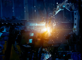 Fototapeta na wymiar Large factory robotic arms are spraying sparks to weld car frames