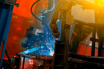 Large factory robotic arms are spraying sparks to weld car frames