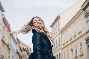 Fototapeta premium street style portrait of european attractive blonde woman wearing leather trousers and jacket. crossing the street and smiling at camera. fashion outfit details perfect for autumn fall winter