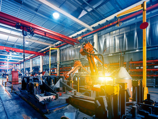 Large factory robotic arms are spraying sparks to weld car frames