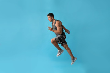 Athletic young man running on light blue background, side view