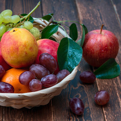 red grape berries and fresh fruits in a straw basket on a dark wooden background.