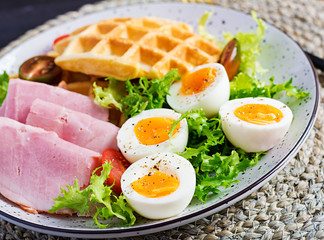 Breakfast with cornmeal waffles, boiled egg, ham and tomato on dark background. Appetizers, snack, brunch. Healthy food.