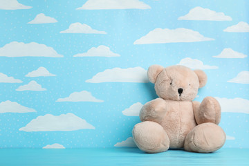 Teddy bear on wooden table near wall with painted blue sky, space for text. Baby room interior