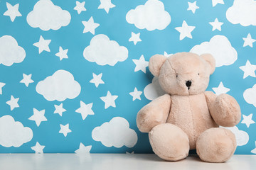 Teddy bear on white wooden table near wall with painted blue sky, space for text. Baby room interior