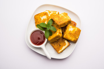 Amritsari Paneer Tikka made using cottage cheese cubes dipped in a batter made with besan, chat masala and spices and shallow fried in pan, served with ketchup