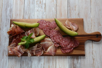 Salami, prosciutto, bacon served with melon and mint on the cutting board. Italian lunch Delicatessen assortment of cold meat
