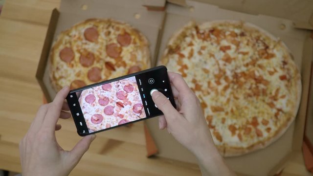 Female Food Blogger Taking Photos Of 3 Pizza By Smartphone In Pizzeria. Photographing Food For Social Network. Woman Hands Taking Picture of Delicious Pizza With Cellphone on Wooden Table in Kitchen.