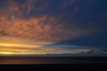 beautiful evening blue sky with golden clouds, dark almost black water, city silhouette and lights shine in the distance