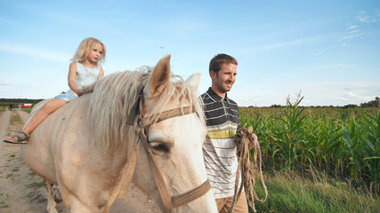 Father rides a little daughter on a white horse.
