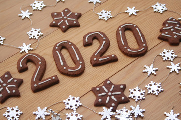 New Year's Eve background. Homemade chocolate cookies in shape of  2020 on a wooden table with pine branches and silver stars