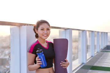 Beautiful woman with a yoga mat and water bottle outdoor.