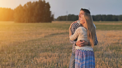 Young husband and wife cuddle at sunset and look towards the sun